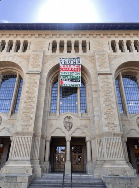 A picture of Green Library with a banner hanging on it hat read, “Levin and Martinez / Don’t cower to Trump / Drop the Charges / Invest in Students / Divest from Genocide."